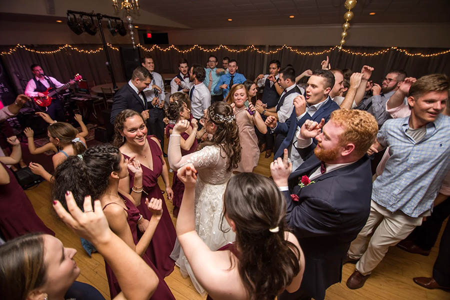 A bride is surrounded by her guests on the dance floor while The Boston Premier Band plays dance music at her wedding.