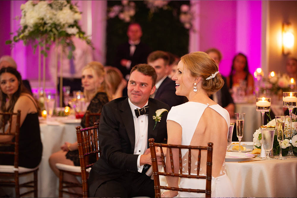 A bride and groom listening intently as the best man gives a toast.