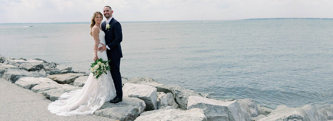 A bride and groom posing by the sea shore before their reception in Bristol, RI