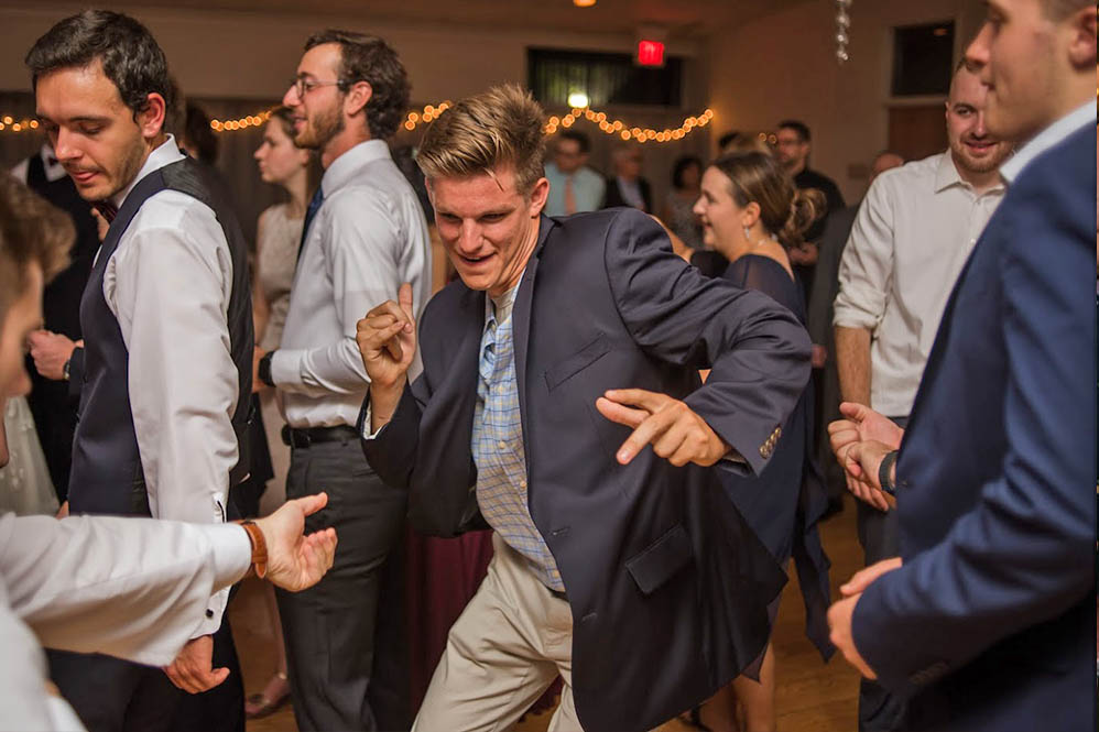 A young man dances wildly as he hears his favorite song at the wedding.