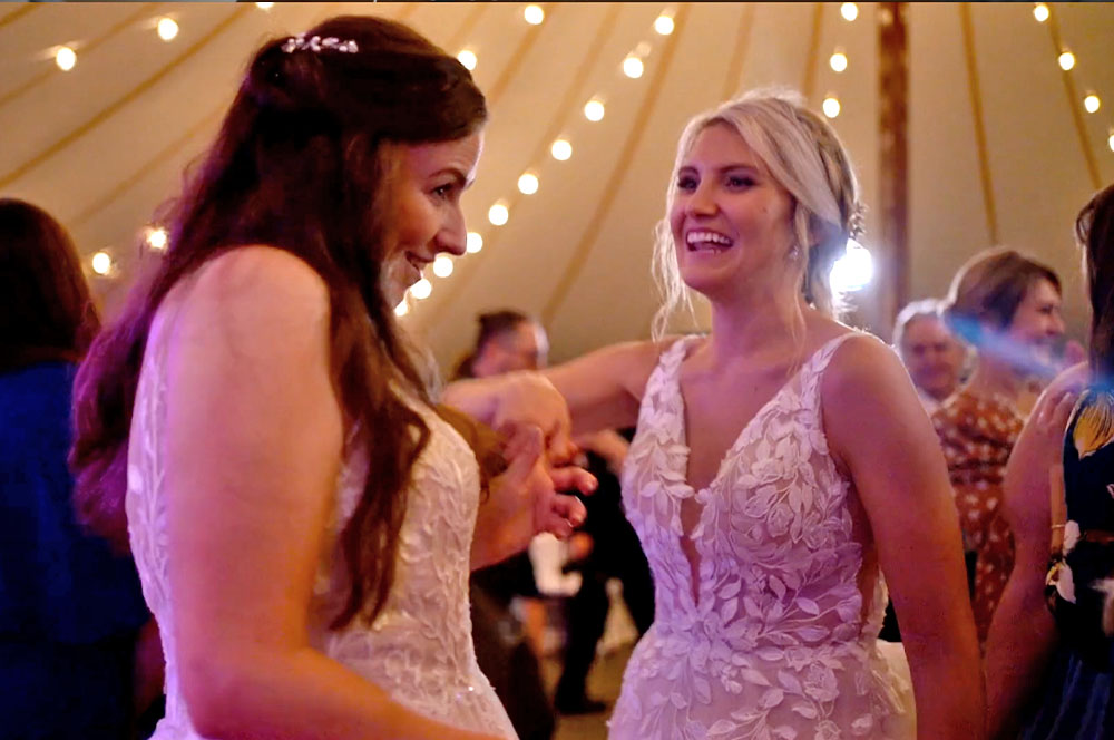 Two brides smiling while they dance to the boston premier wedding band.