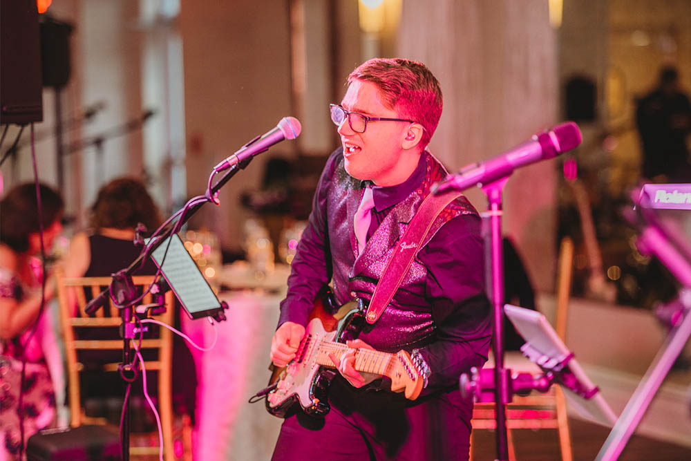 Boston Premier's guitarist on stage under brightly colored lights at a wedding.