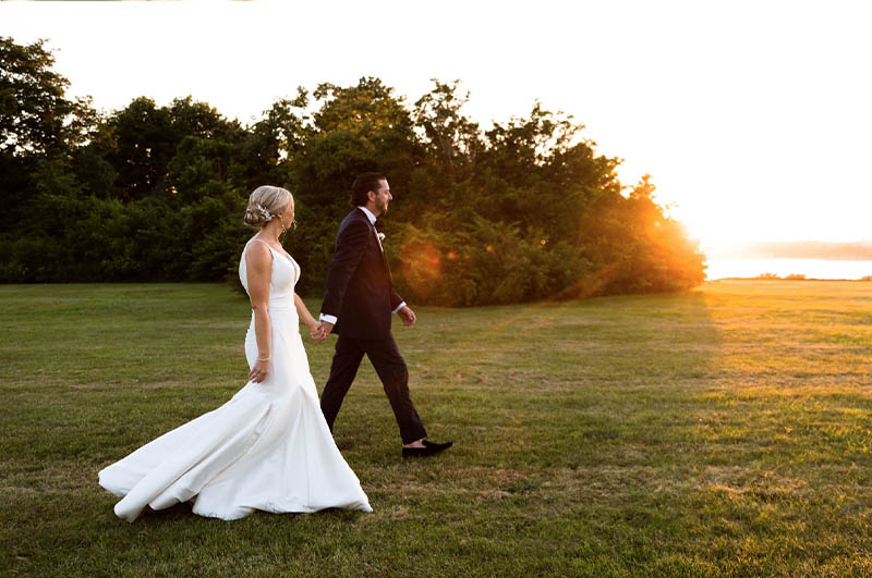 The bride and groom walking hand in hand as the sun sets in the distance.
