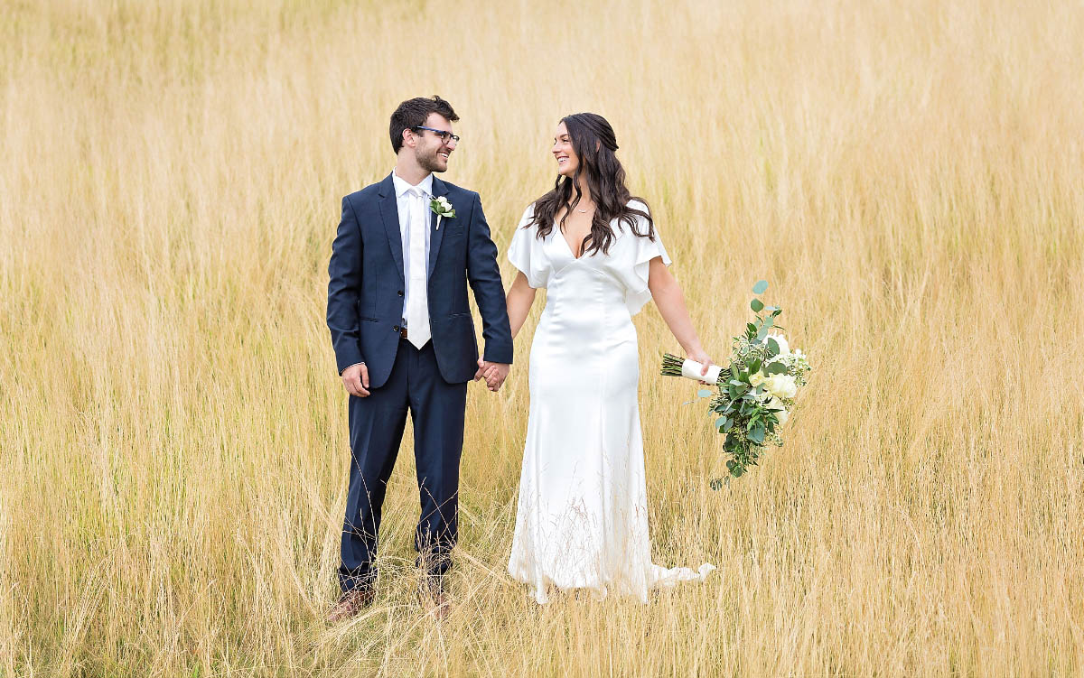 The bride and groom standing in a field of golden grass.