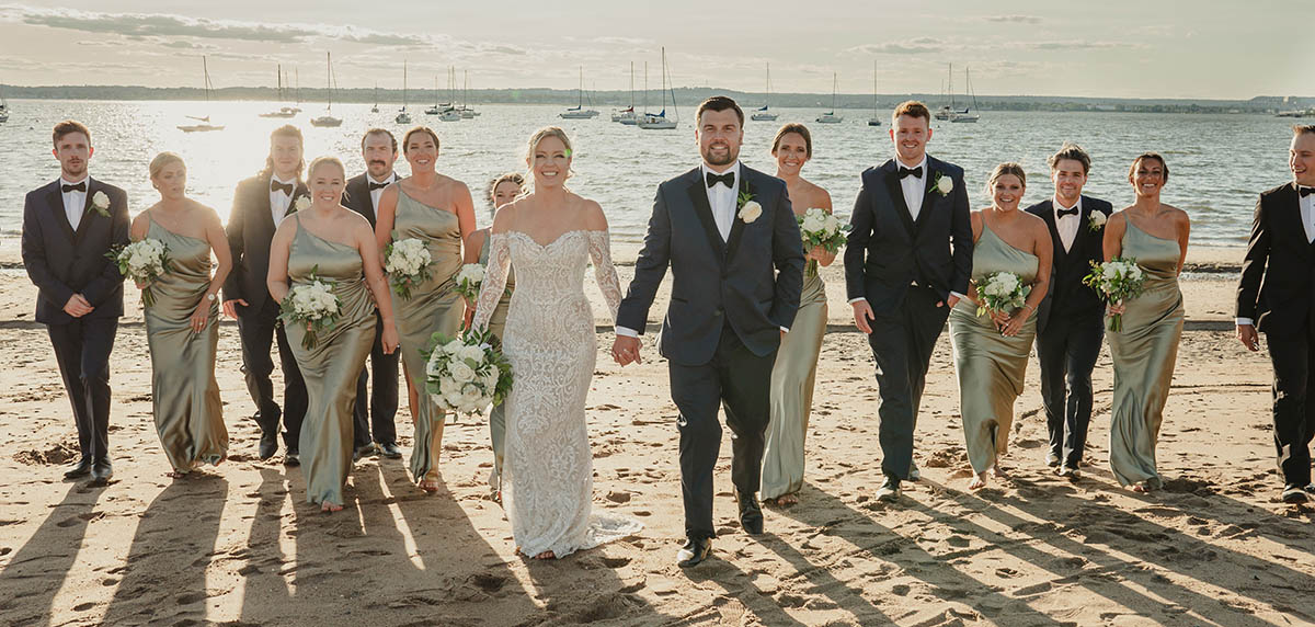 The bride and groom stroll the beach with their bridal party at Anthony's Ocean View