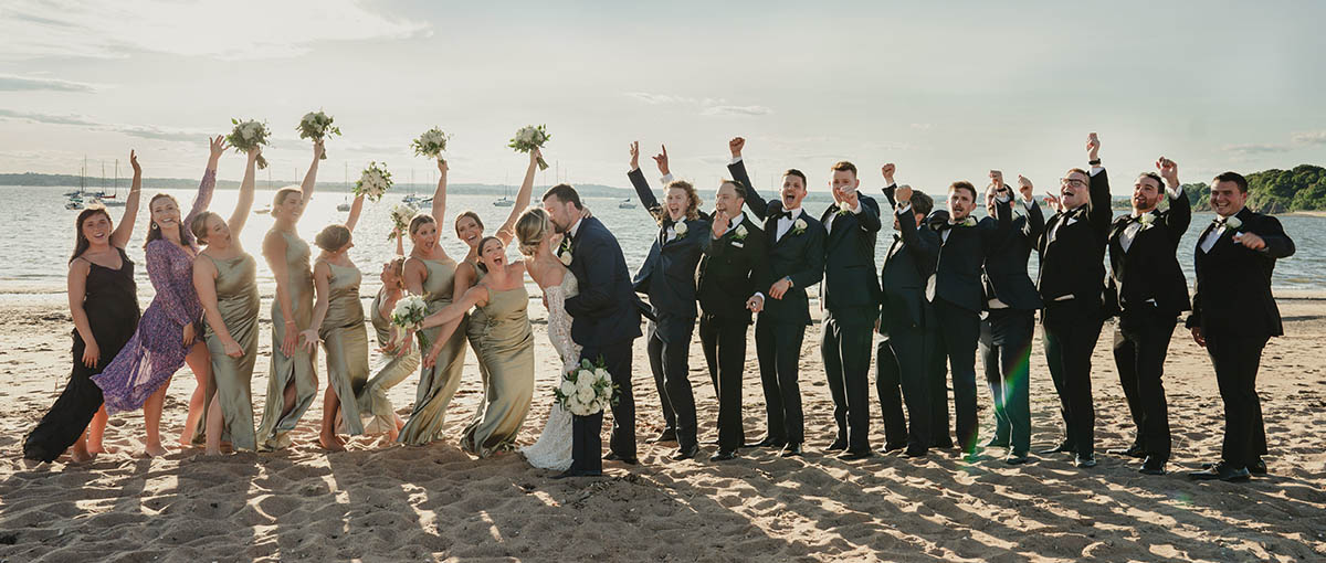 The bridal party cheer as the bride and groom kiss.