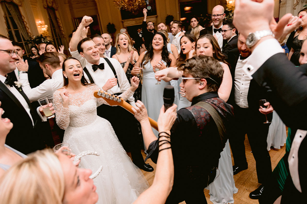 A bride and groom cheer as a guitarist performs a solo on the dance floor.