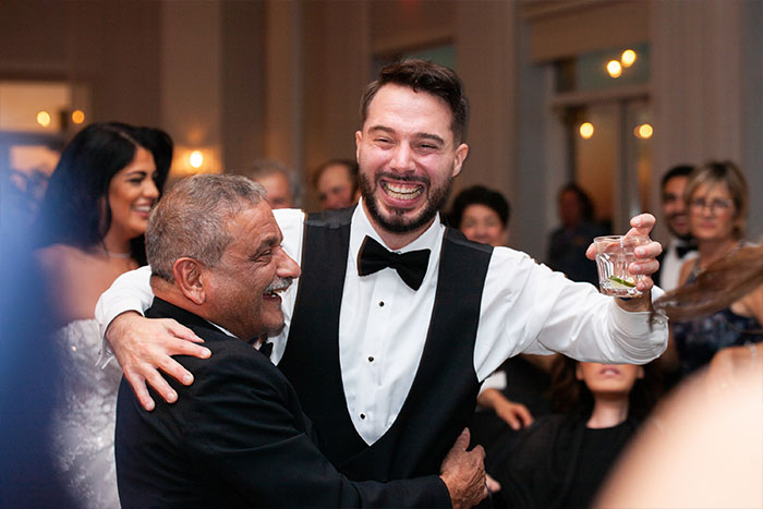 A groomsman smiling as he dances with the father of the groom.