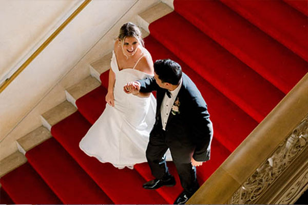 The Bride and Groom walking down a red carpeted staircase.